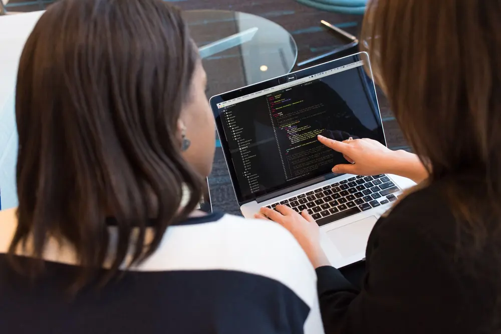 Duas pessoas revisando código em um notebook